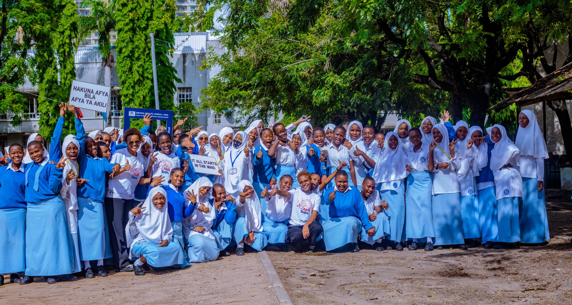 Mental Health Africa school outreach — students holding 'Hakuna Afya Bila Afya Ya Akili' and 'It All Starts In The Mind' signs